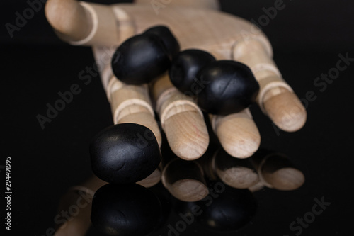 Group of four whole tasty black olive with wooden hand isolated on black glass