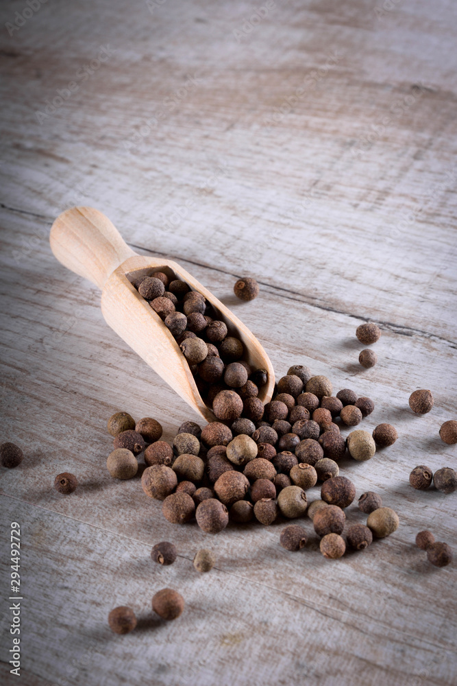 Pepper peas in a wooden spoon on a wooden background. Spices are scattered on the table Pepper peas in a wooden spoon on a wooden background. Spices are scattered on the table