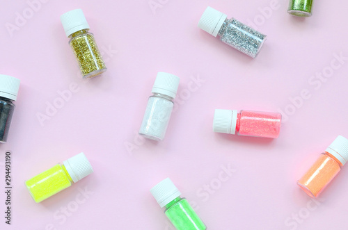 A flat lay pattern with colorful glitter bottles lies on pastel pink background