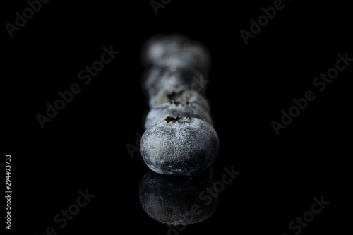 Group of five whole fresh blue blueberry isolated on black glass photo