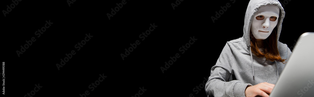 panoramic shot of anonymous internet troll in mask using laptop isolated on black panoramic shot of anonymous internet troll in mask using laptop isolated on black