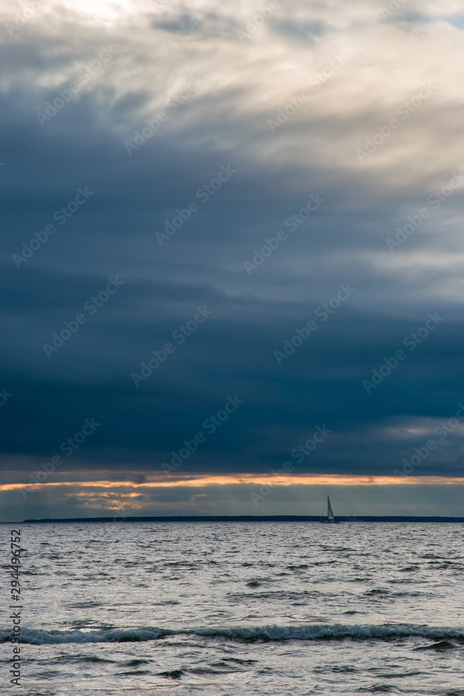 Beautiful seascape with heavy clouds and a small yacht. Windy, gloomy, small waves. Vertical frame.