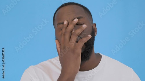 Portrait of annoyed bearded man covering face like facepalm expressing frustration or shame, over blue background. Concept of emotions 4K