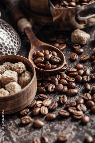 Coffee beans in wooden spoon on dark textured background.