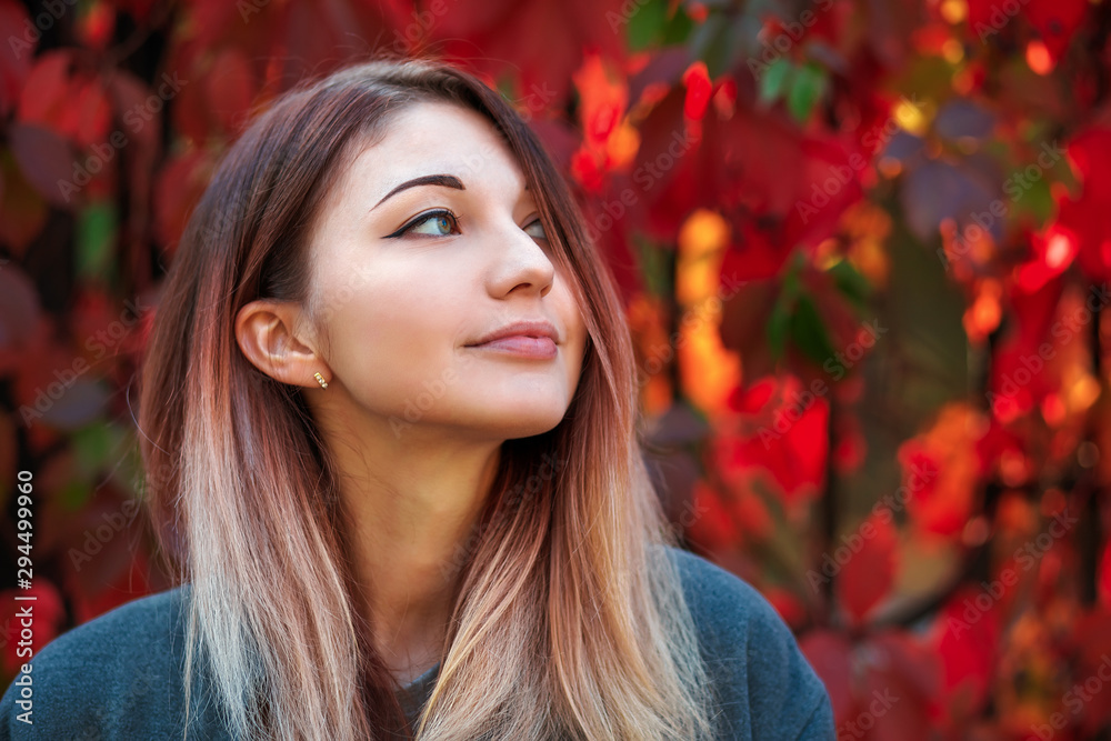 Dreamy beautiful girl with long colorful hair on autumn background of red grape hedge. Inspired woman in gray coat. Autumn euphoria. Female emotional portrait in faded tones. Dreamy beautiful girl with long colorful hair on autumn background of red grape hedge. Inspired woman in gray coat. Autumn euphoria. Female emotional portrait in faded tones.