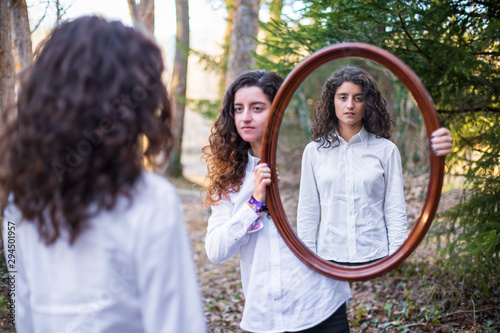 young woman showing reflection of twin sister in autumn day in the forest