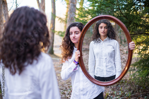 young woman showing reflection of twin sister in autumn day in the forest