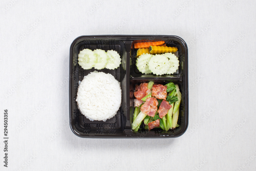 Stir Fried Kale with Bacon with Rice put in black plastic box, put on a white tablecloth, food box, Thai food.