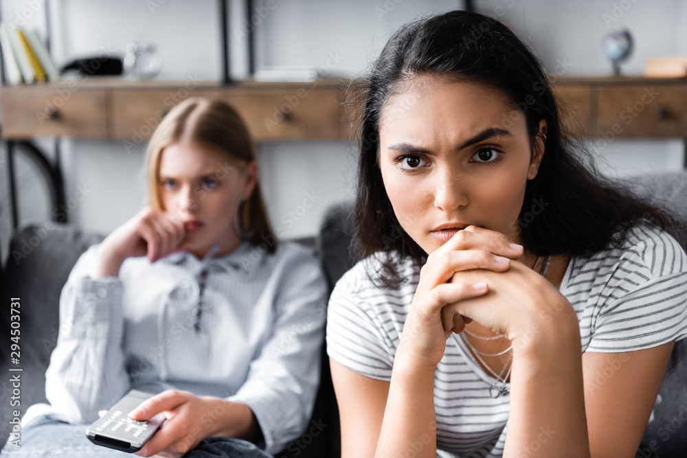 multicultural friends holding remote controller and looking away in apartment