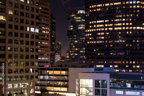 Night scene of a dense cityscape of modern high rise buildings and skyscrapers with glowing windows - concepts of business, economy, jobs, work, employment