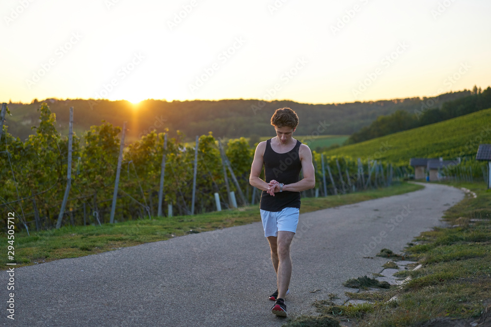 runner in shorts looking at his watch in sunset green nature in background