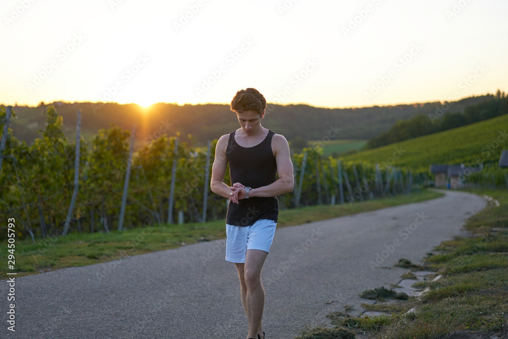young runner in shorts looking at his watch in sunset