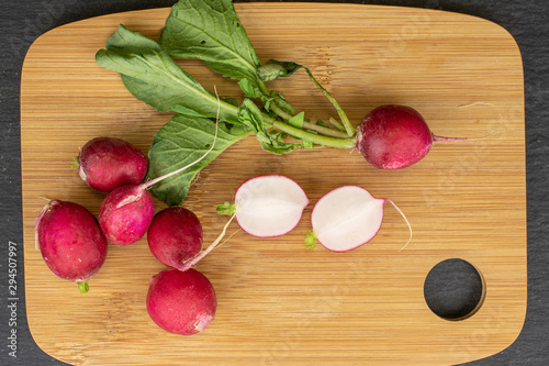 Group of five whole two halves of fresh red radish on bamboo cutting board flatlay on grey stone