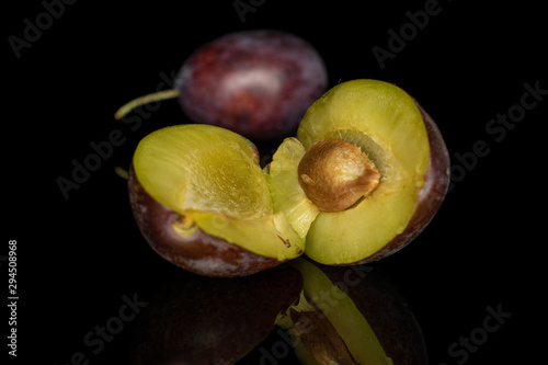 Group of one whole two halves of sweet purple plum isolated on black glass