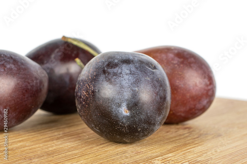 Group of four whole sweet purple plum on bamboo cutting board isolated on white background