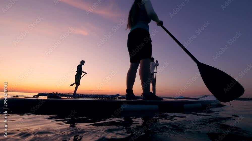 Athletes supping with paddles on water.