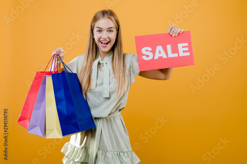 happy smiling pretty young woman with sale sign and colorful shopping bags isolated over yellow