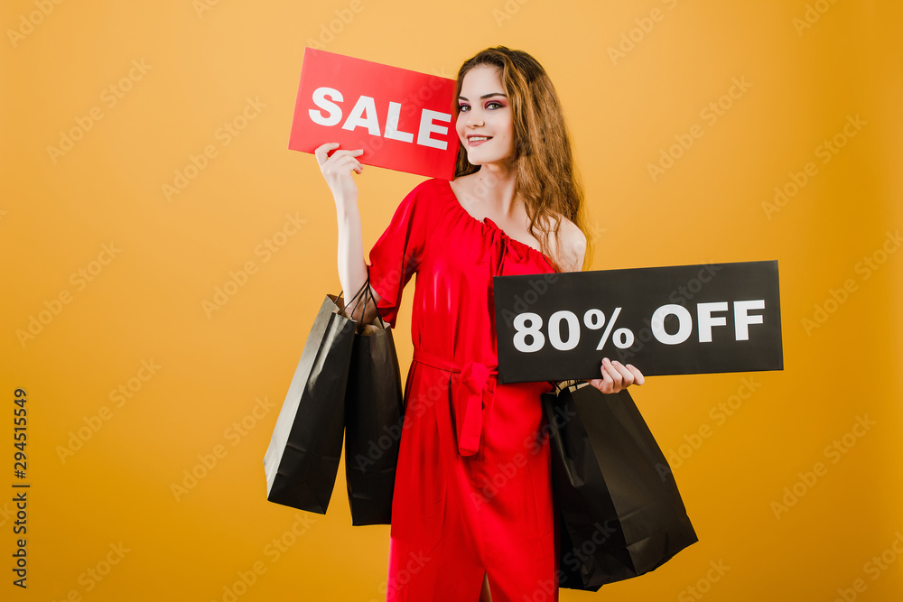 young woman in red dress with sale 80% sign and paper shopping bags isolated over yellow