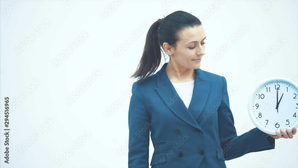 Young good teacher standing on a white background. Holds a white clock and drinks water from the glass. Young good teacher standing on a white background. Holds a white clock and drinks water from the glass.