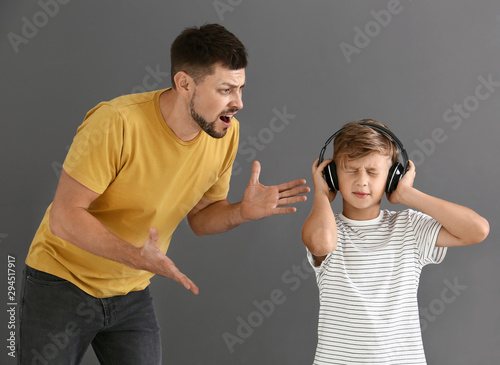 Little boy with headphones ignoring his angry father against grey background