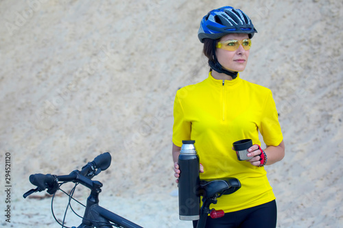 Beautiful girl cyclist in yellow with tea and thermos in hand