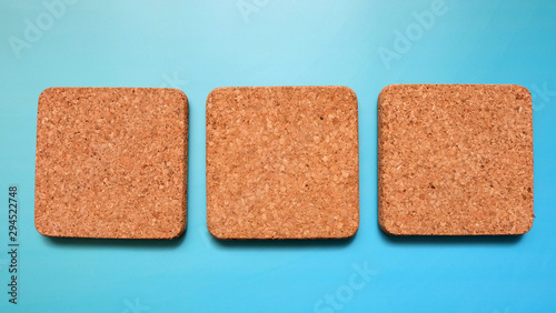 3 square cork tiles arrange in a row next to each other, with a blue background.