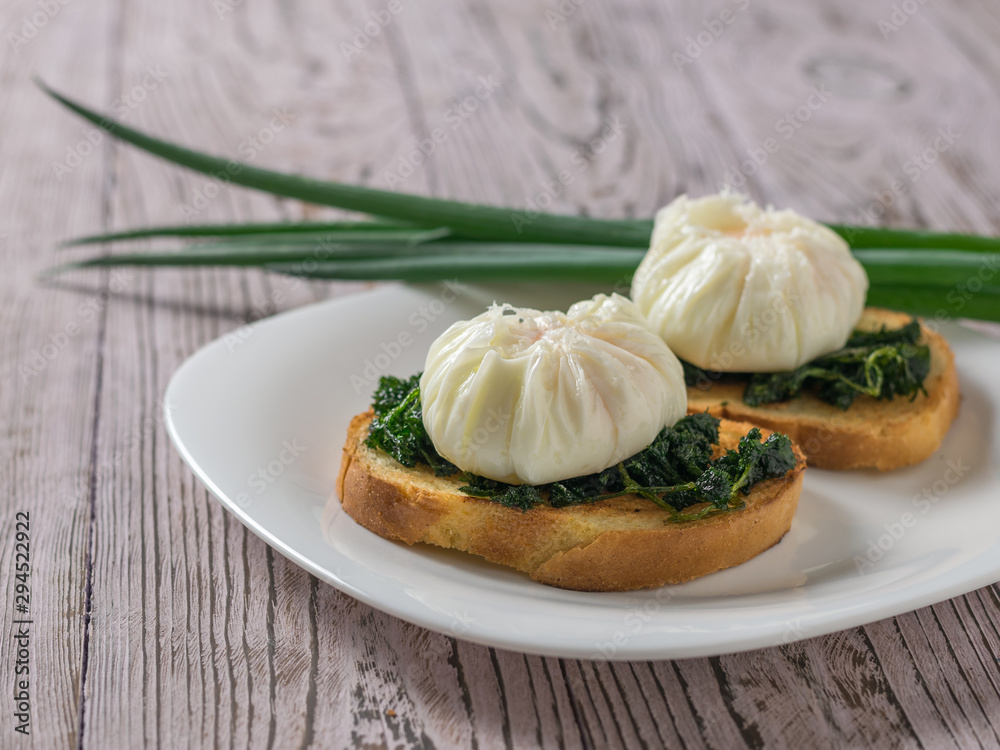 Two poached eggs with bread and green onions on a wooden table.
