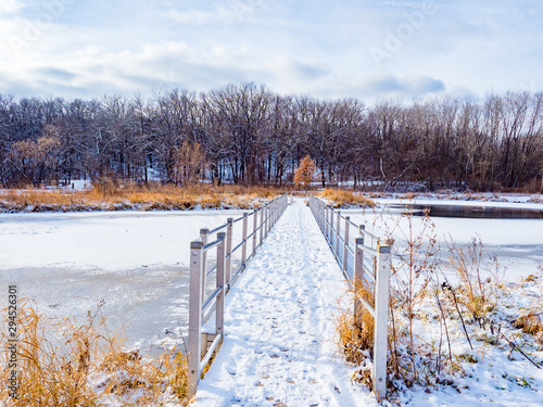 Foot bridge over icy lake, snowy forest and trail in Quarry Hill Nature Center, Rochester, Minnesota on a snowy day photo