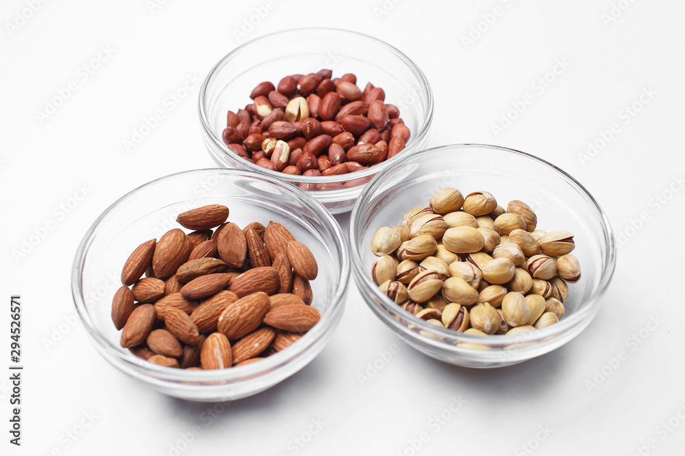 peanuts, almonds and pistachios in bowls on white background peanuts, almonds and pistachios in bowls on white background