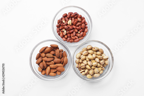 peanuts, almonds and pistachios in bowls on white background