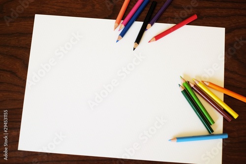 Many colored pencils and white paper on wooden table with free space for text.