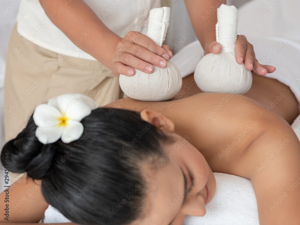 Beautiful young asian woman lying on the bed having a massage with herbal compresses in a spa. Thai massage for health. Select focus hand of masseuse Beautiful young asian woman lying on the bed having a massage with herbal compresses in a spa. Thai massage for health. Select focus hand of masseuse