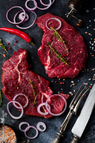 Two Raw beef steak with spices, onions and chili on dark slate or concrete background. Top view