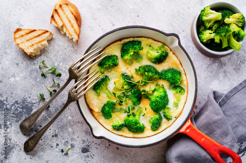 Omelette with broccoli and green young onions on red cast iron pan on old gray concrete background. Top view.