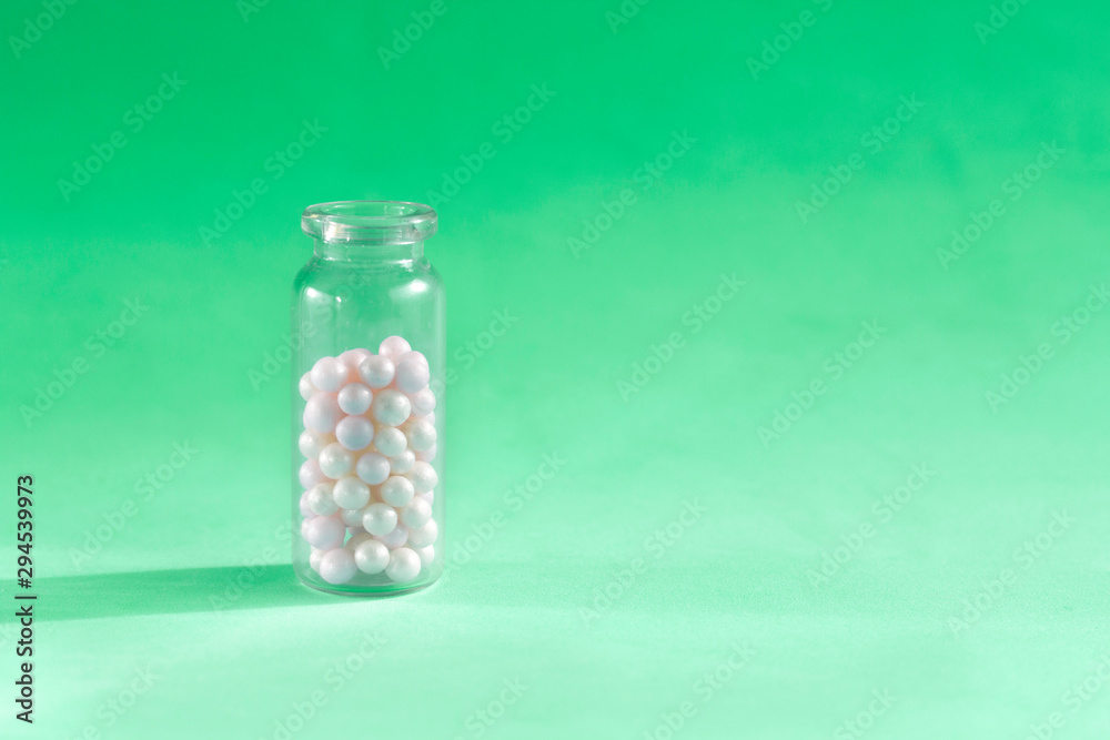 Homeopathy pills in teaspoon on green background. Homeopathic medicine globules - herbal remedy alternative medication.