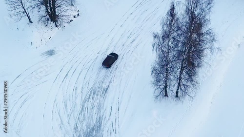 A loud black car race drifting in the icy snow around trees of the road course. A steady overhead following shot of a car drift racing a road course photo