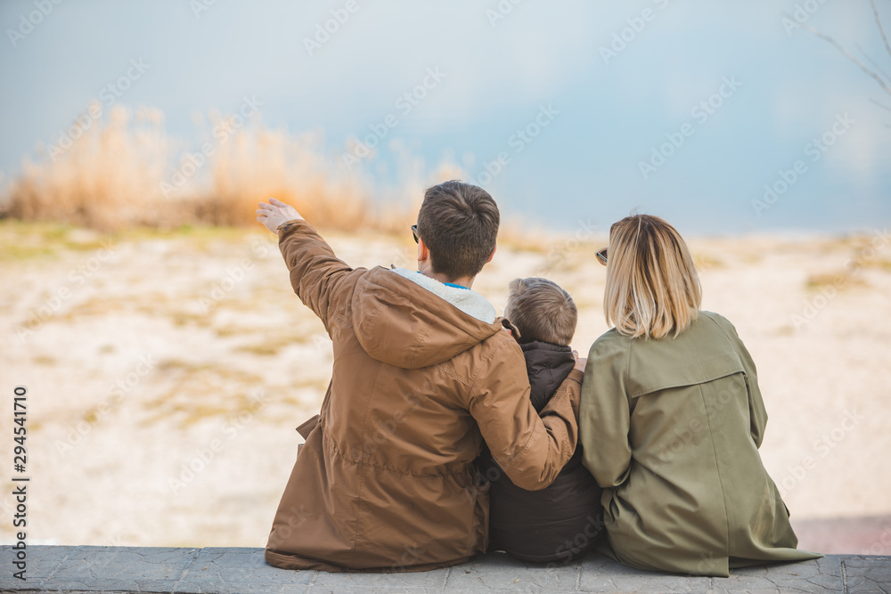 young beautiful family sitting at beach with view lake - obrazy, fototapety, plakaty 