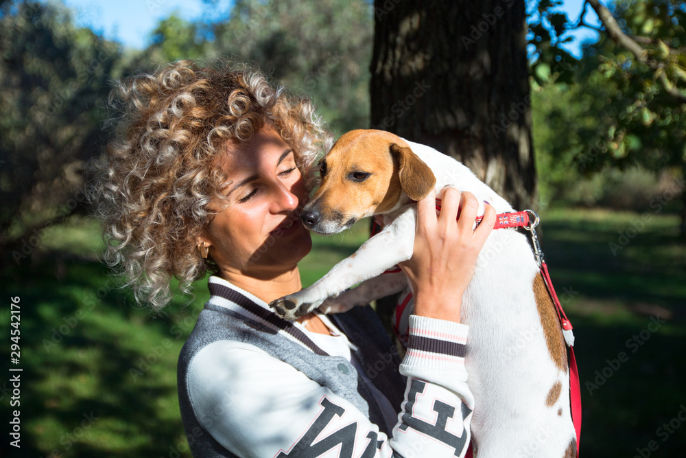 beautiful blonde curly girl plays with her pet, jack russell dog in the green autumn park