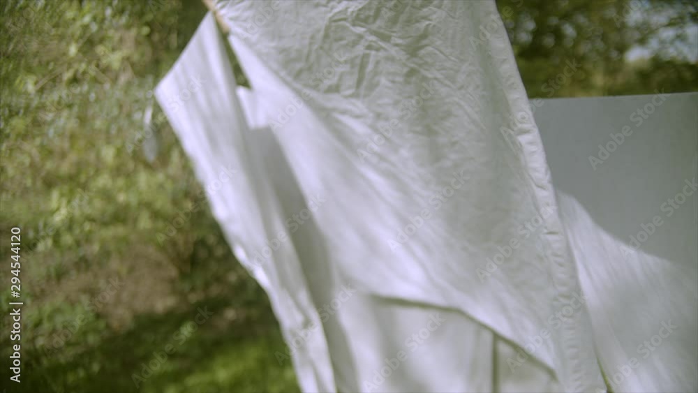 White laundry sheets on the line sway in wind, slow motion. 