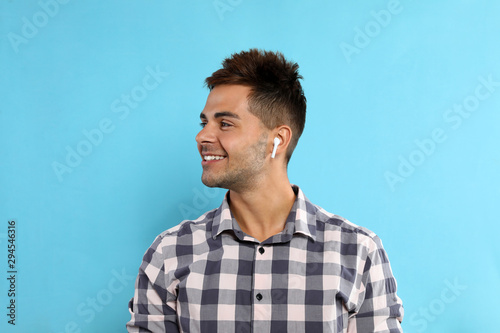 Happy young man listening to music through wireless earphones on light blue background