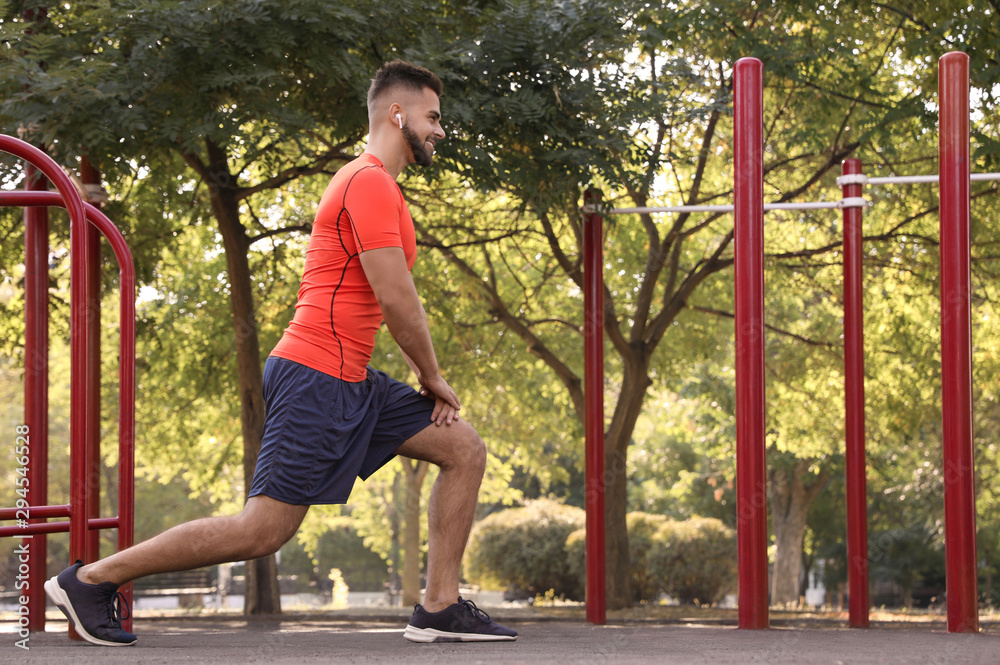 Fototapeta premium Young man with wireless headphones listening to music while exercising on sports ground. Space for text