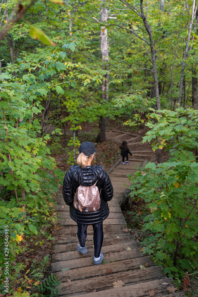 Mother and child going down steps in forest in autumn in park, Seen from behind, telephoto lens. Gatineau Park, Quebec, Ontario. Mother and child going down steps in forest in autumn in park, Seen from behind, telephoto lens. Gatineau Park, Quebec, Ontario.