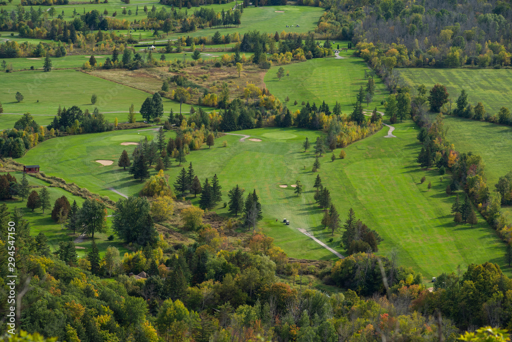 Golf course seen from above during autumn, with pine trees and other trees turning red and orange. Quebec, Canada