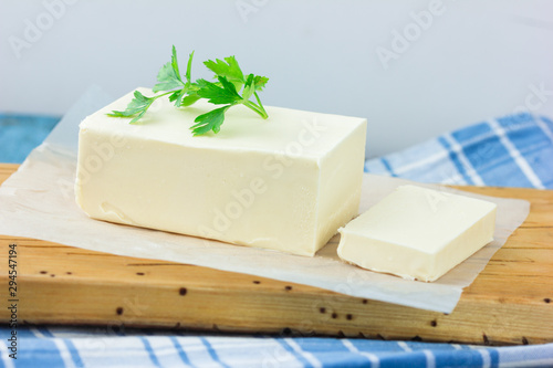 A few slices of yellow butter cut off from a just opened pack of butter with a knife on a brown wooden cutting board.