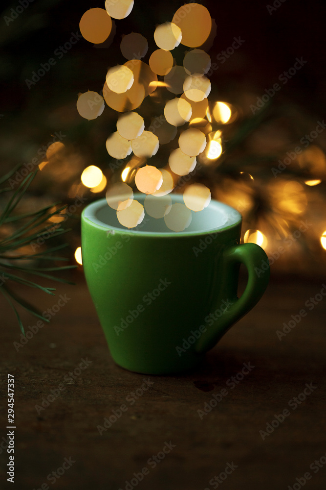 Obraz premium Coffee cup over Christmas lights bokeh in home on wooden table with tree. 