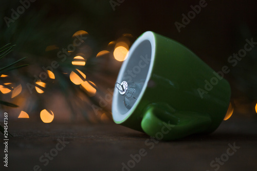 Coffee cup over Christmas lights bokeh in home on wooden table with tree. 