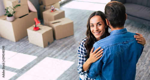 Her dazzling smile. A woman is hugging her boyfriend in their new flat with a smile, which reflects her sheer happiness.