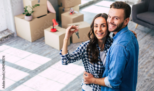 Happy housewarming. A young couple holds happily a key to their new home which they were so excited about, and this can't but make them feel overwhelmed with positive emotions.