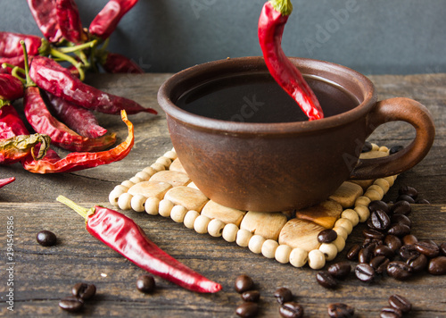 Hot pepper pod in a cup with hot coffee. Coffee beans and star anise on a saucer. Wooden background. photo