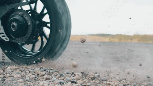 The pebbles bounce off the ground due to the rapid slippage of the motorcycle wheel. Close up slow motion footage. 4k.
